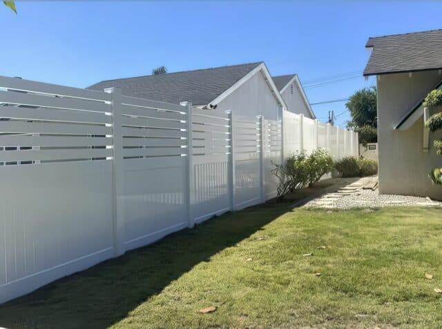 Vinyl privacy and picket fence connecting to the taller full privacy fence leading into the backyard with small plants