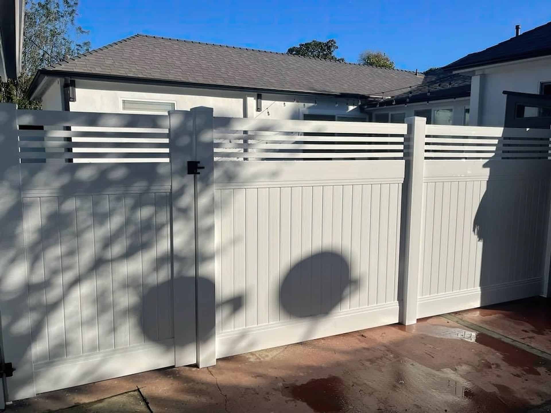 Vinyl privacy and picket fence with gate allowing entrance into ranch style home with concrete yard leading up to main door