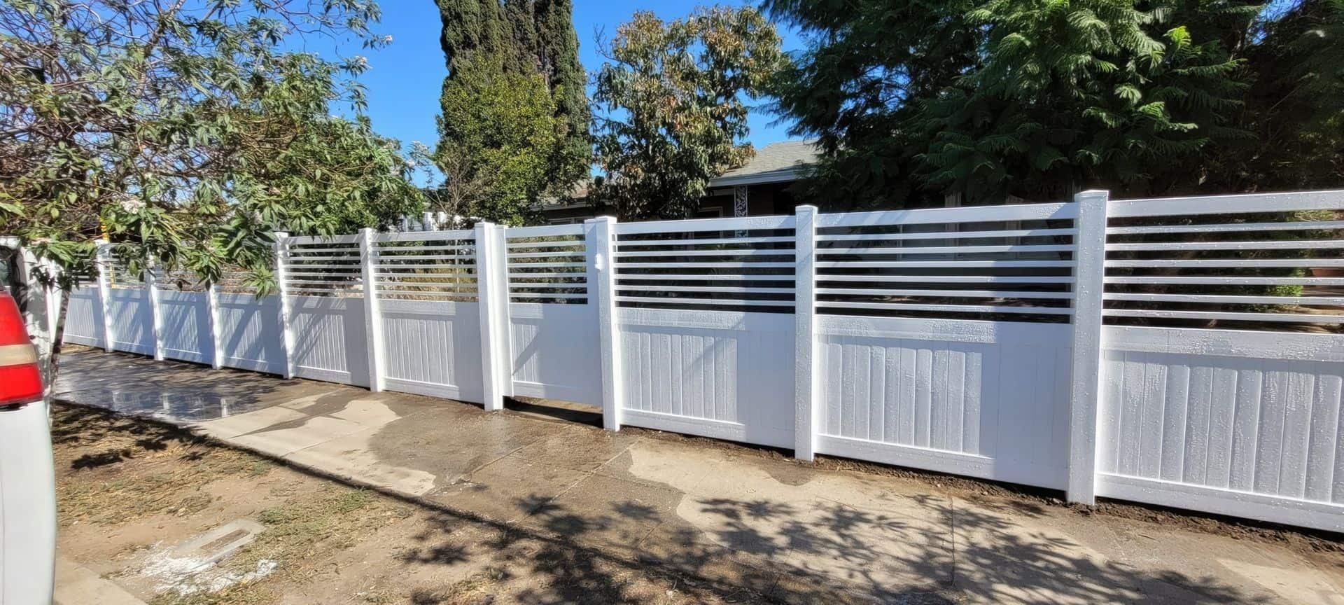 Vinyl privacy and picket fence with horizontal slats and gate leading into front lawn with a multitude of trees and a grassy lawn.