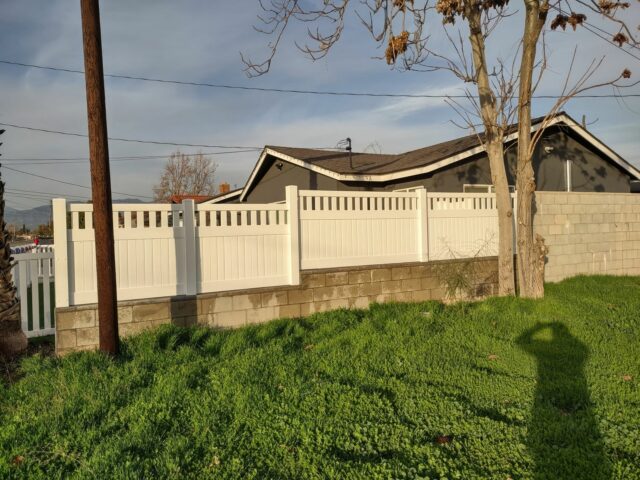 Vinyl privacy and picket fence creating boundary around traditional suburban house and connecting to concrete wall.