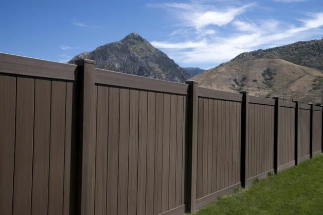 Vinyl privacy fence on lush grassy lawn visually separating suburban house from picturesque hills in the distance