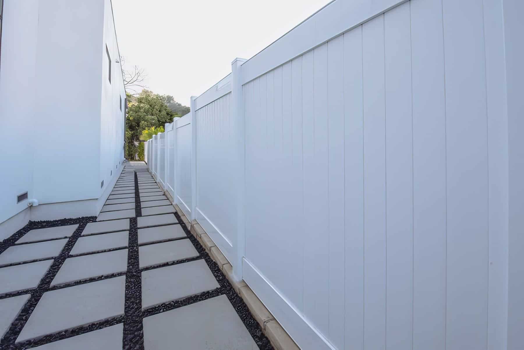 Vinyl privacy fence beside walkway with black stones and tiny black stones surround them against the white paint.