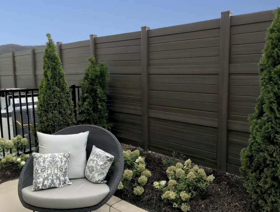 Rich and dark vinyl privacy fence behind small garden with trees and small plants, along with a dedicated relaxing area