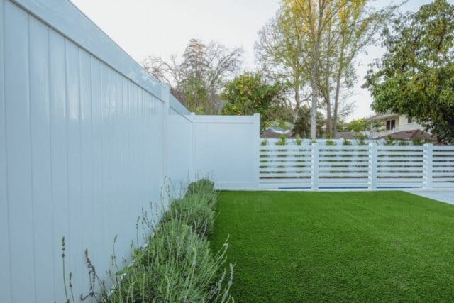Vinyl privacy fence connected to a smaller slatted fence in front of a small garden and surrounding the rest of the home.