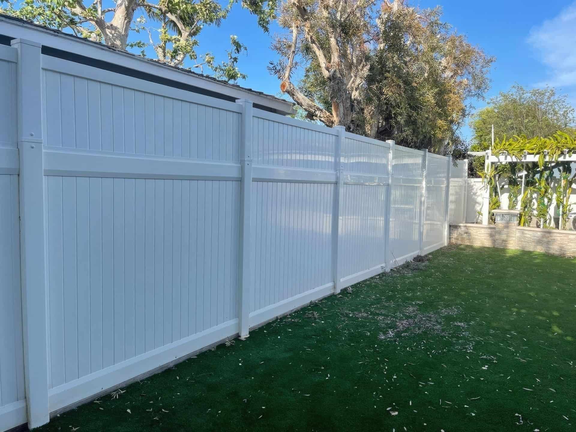 Large vinyl privacy fence separating two houses the from the backyard with a small vertical garden and lush grass.