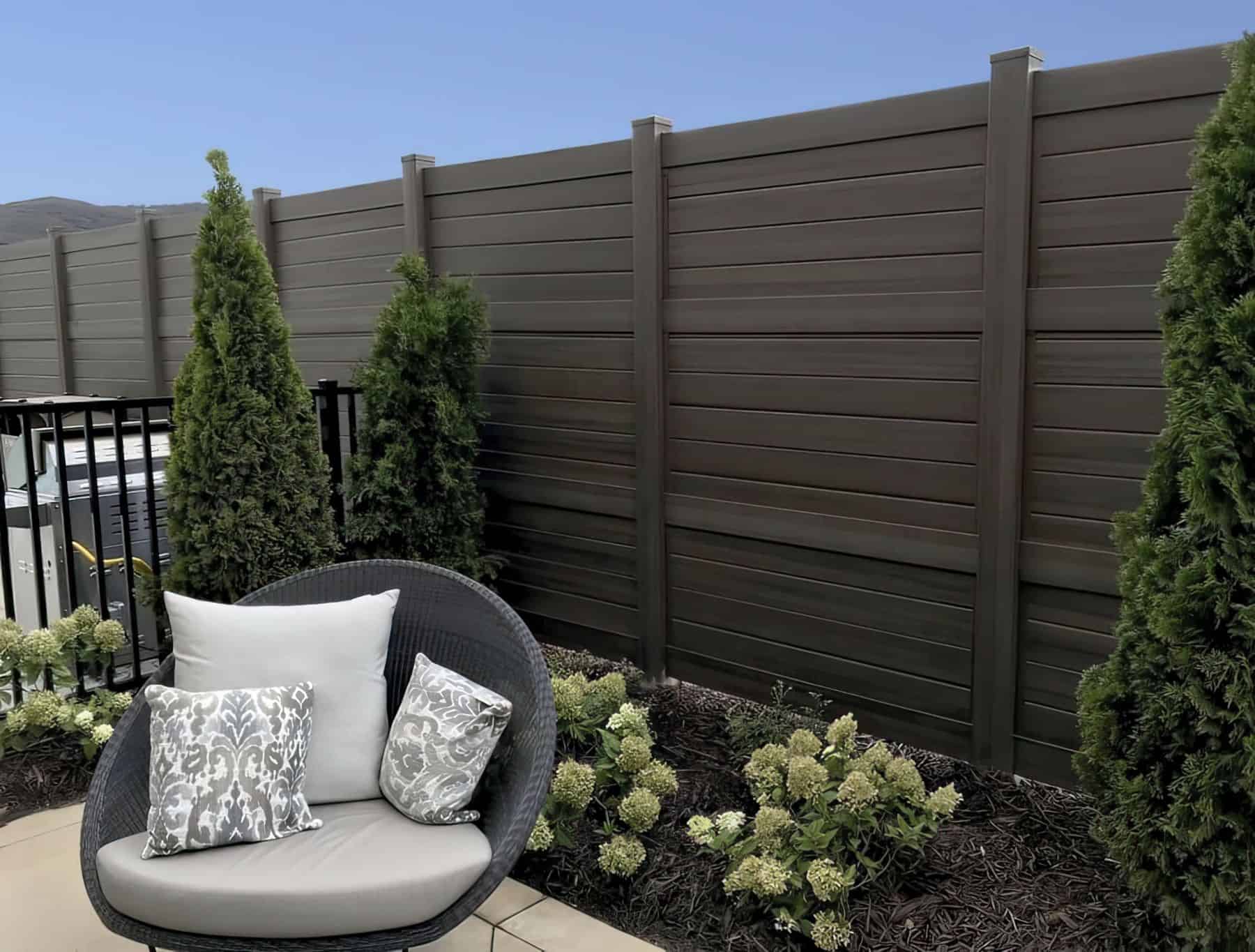 A vinyl privacy horizontal fence behind a small garden with small shrubs and trees in the backyard retreat