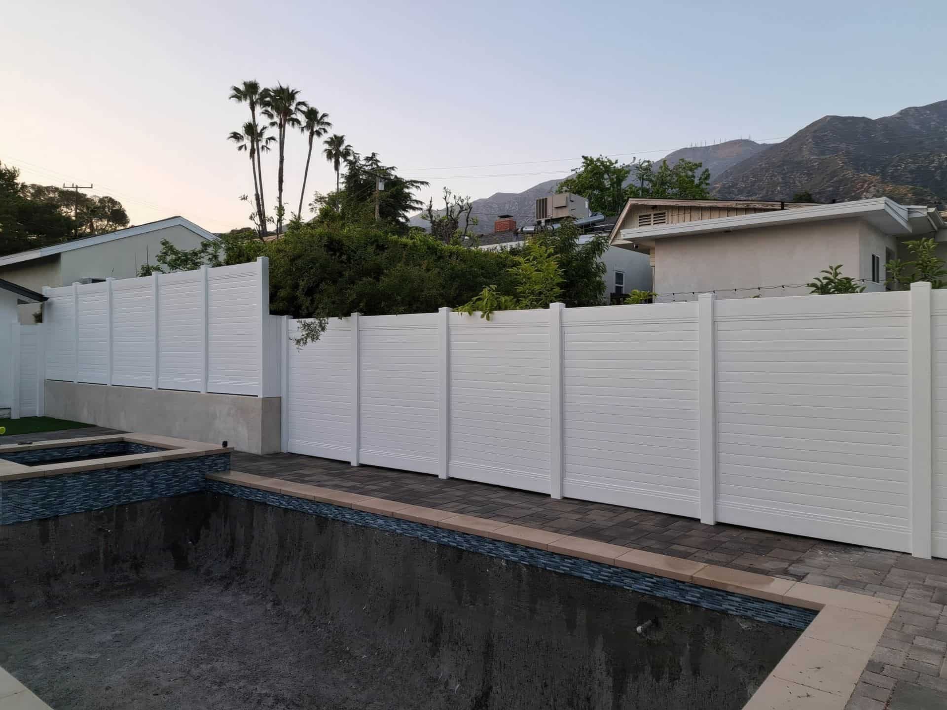 Vinyl privacy horizontal fence creating boundary around swimming pool with jacuzzi and elevated backyard