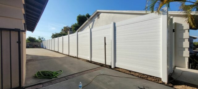 Vinyl privacy horizontal fence creating boundary between two suburban houses with concrete side passage leading to backyard