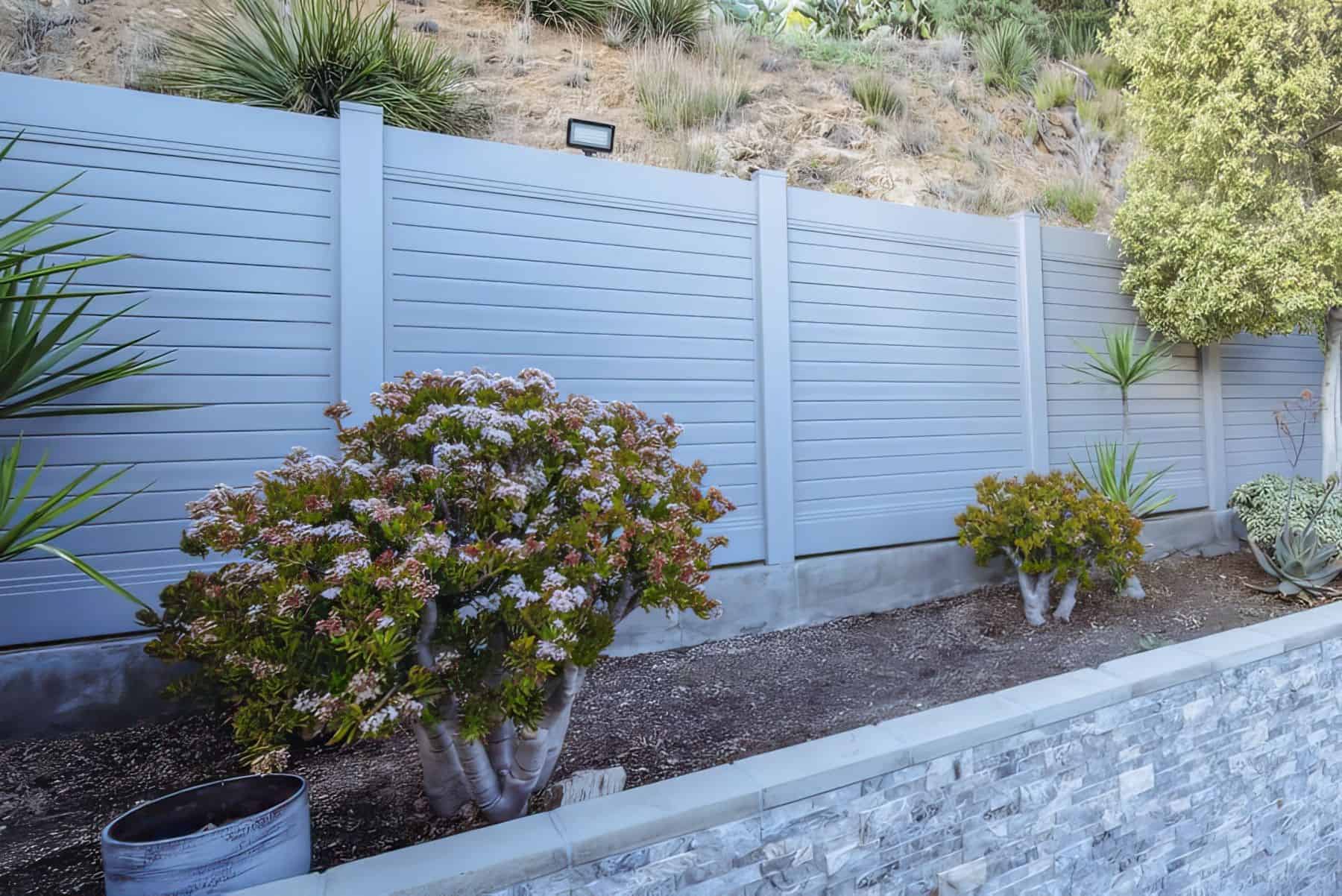Vinyl privacy horizontal fence in front of short hill and behind small backyard garden with miniature trees and small plants