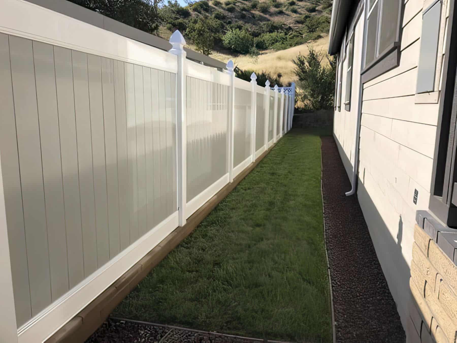 Vinyl privacy two-tone fence in front of small patch of grass within the side passage leading into the backyard.