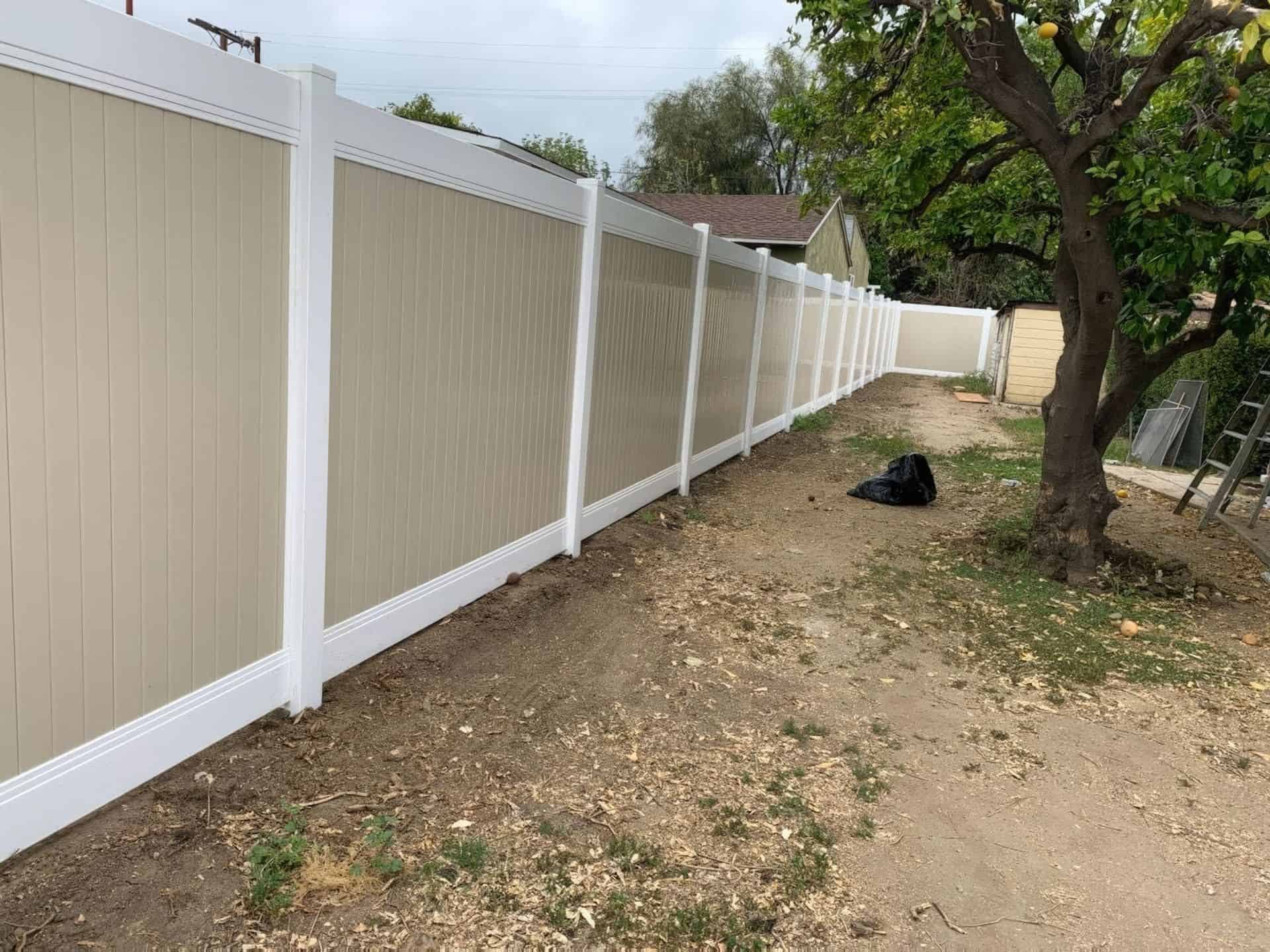Vinyl privacy two-tone fence with beige center and white borders as a boundary around the backyard with a large tree.