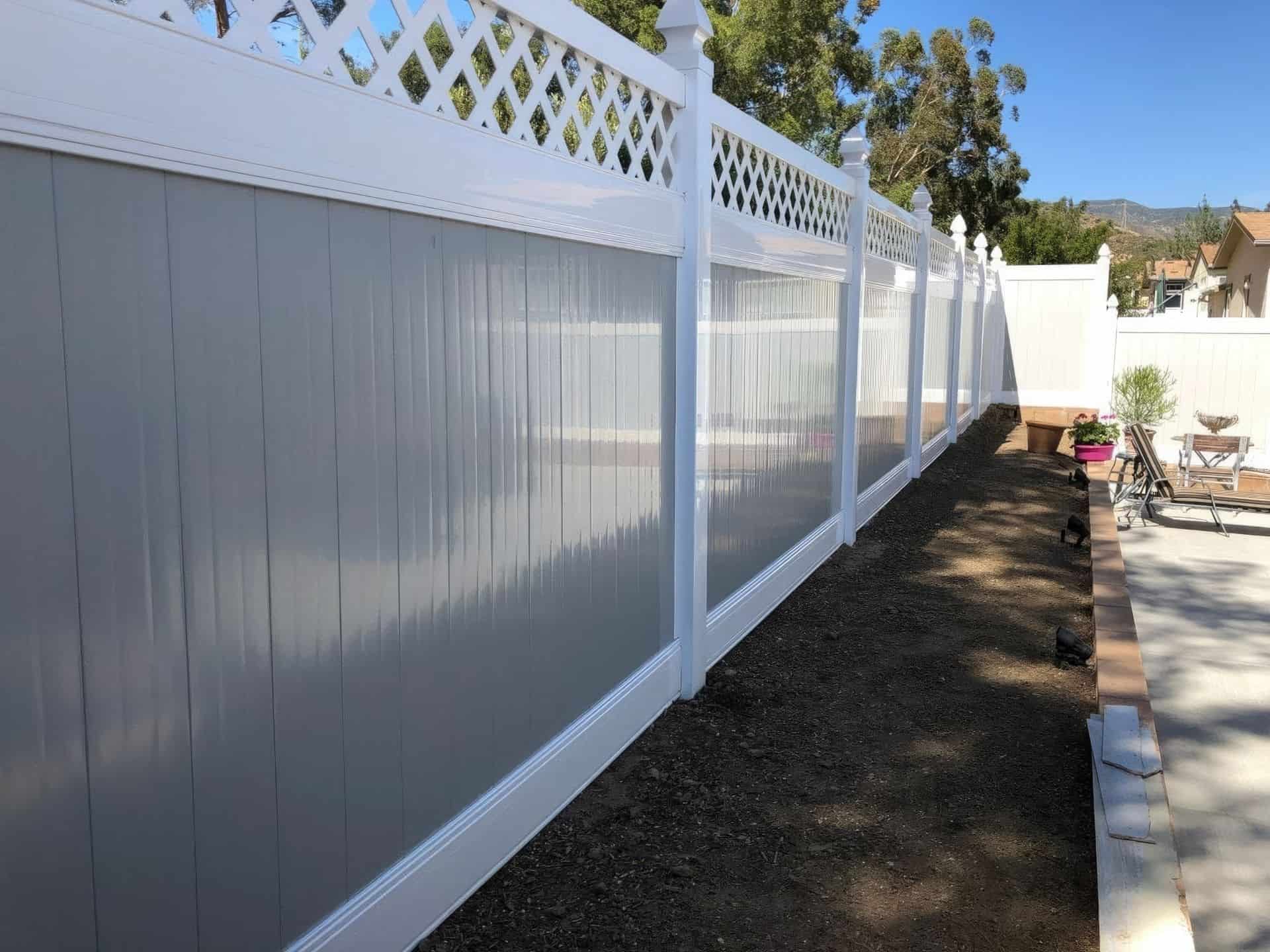 Vinyl privacy two-tone fence with gray center and white border surrounding backyard retreat with small garden and chairs.