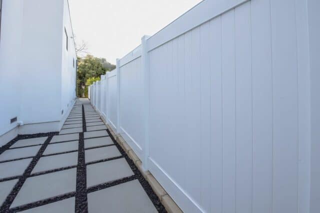 Vinyl privacy vertical fence as boundary wall for side passage with intricately designed walkway with black stones and marble