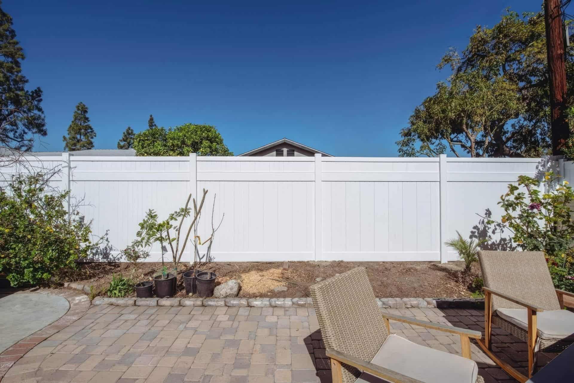 Vinyl privacy backyard fence surrounding backyard red brick oasis with walkway and small garden patch to the side.