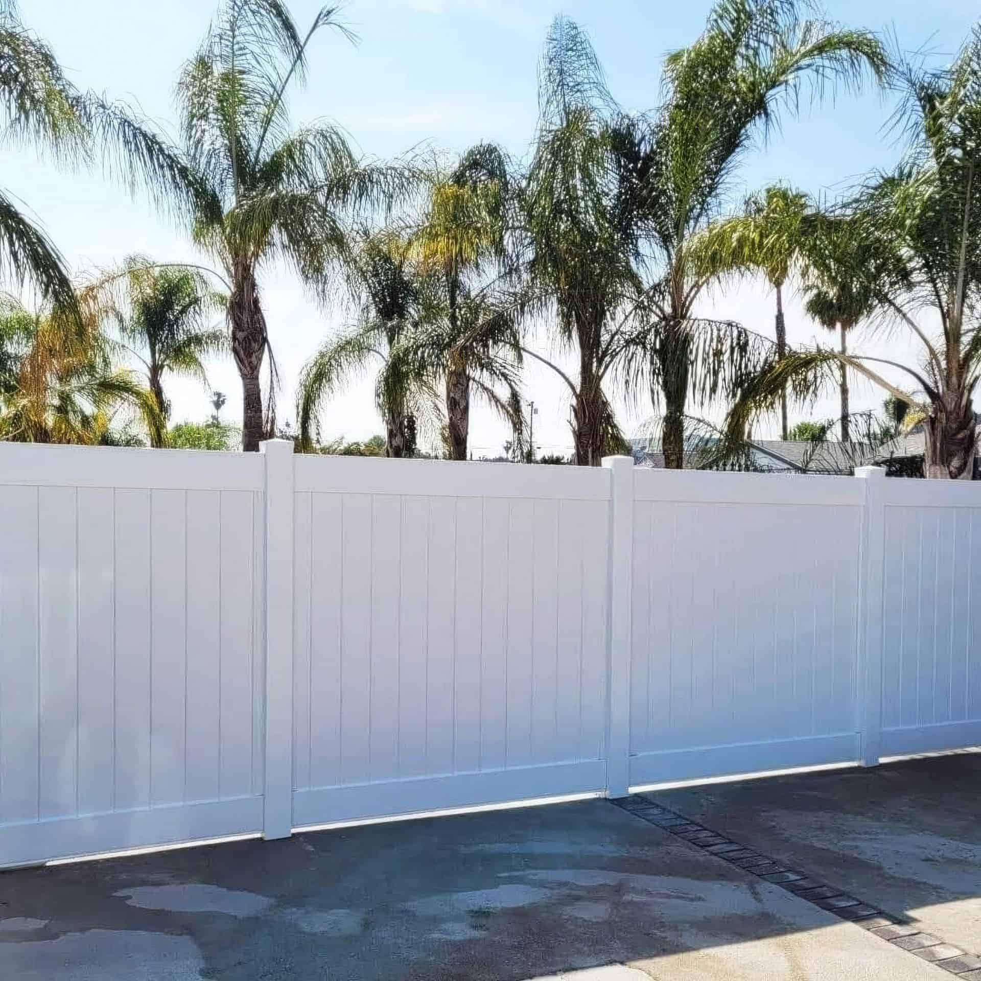 Vinyl privacy vertical fence as boundary wall for home with palm trees in the background and above concrete driveway