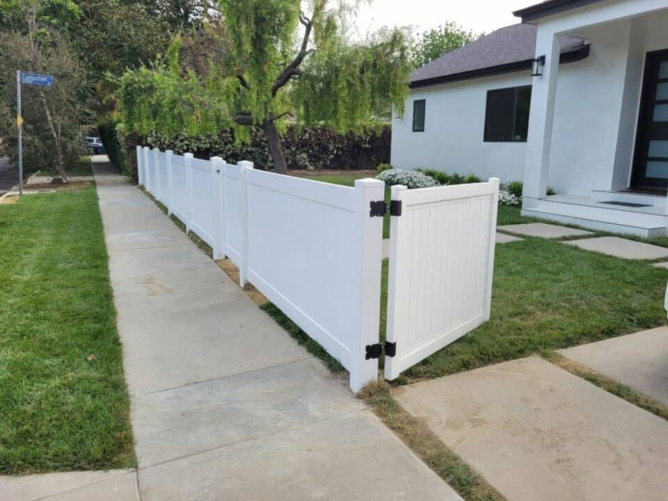 Vinyl privacy vertical fence beside sidewalk, with gate pleading into the front lawn and the main entrance of the house.