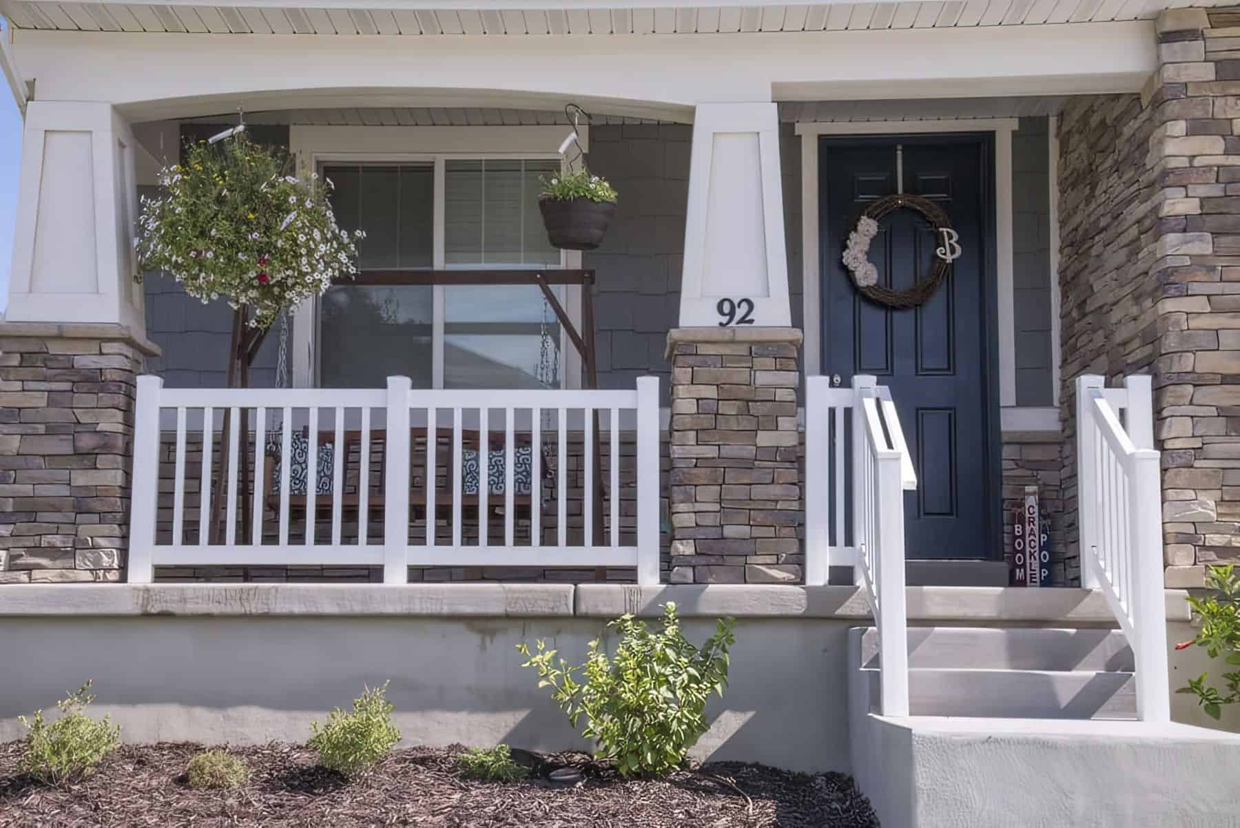 Vinyl rails on small front porch with swing and hanging flowers, and on stairs leading to walkway with small shrubs.