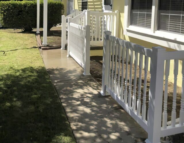 Vinyl rails surrounding small garden area beside lush backyard and steps leading into back door of the house.
