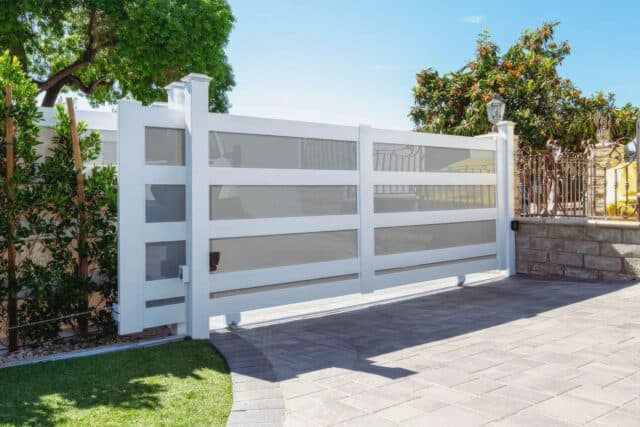 Tall rolling vinyl gate separating concrete driveway from front lawn with vertical garden and lush green lawn.