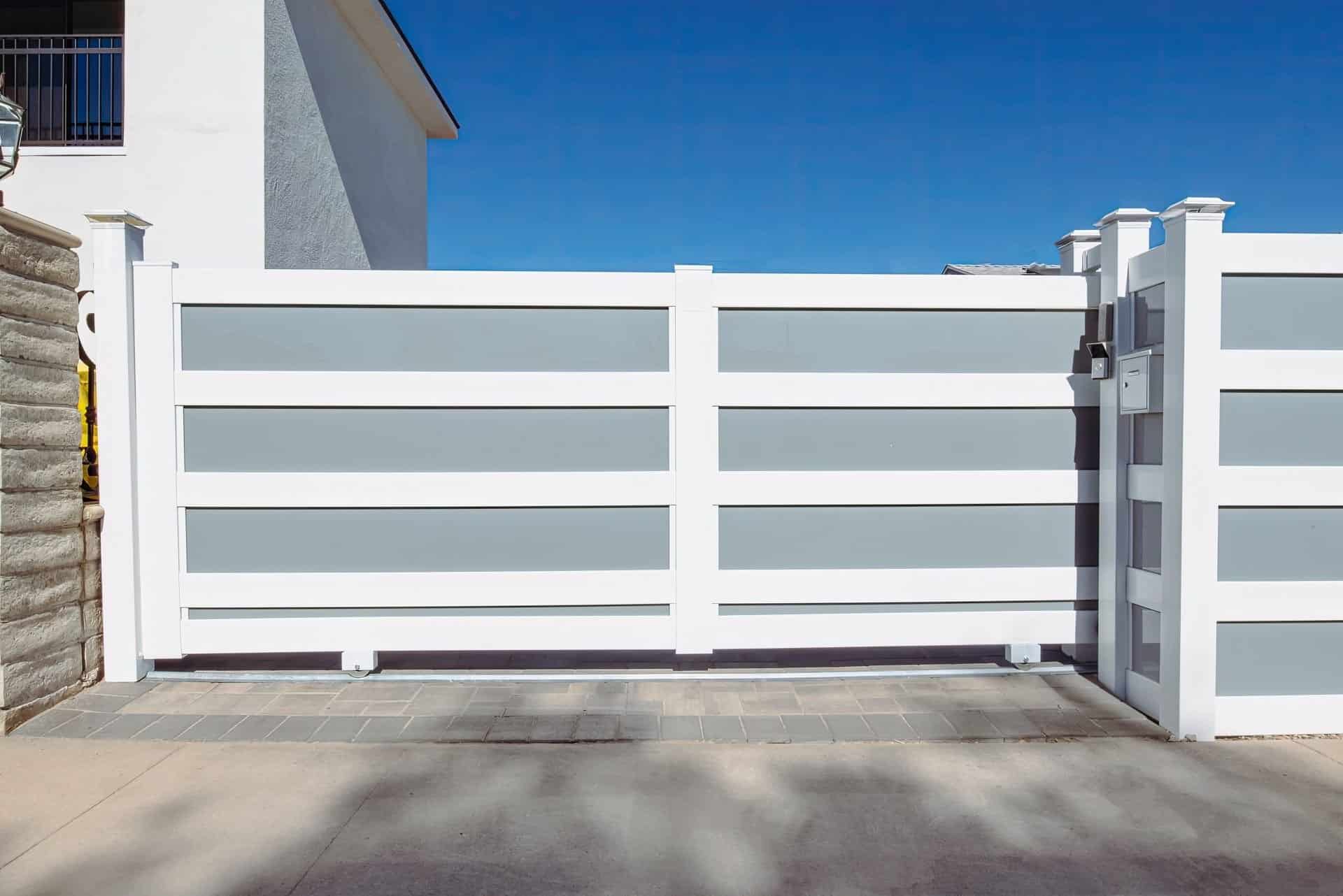 Tall security vinyl rolling gate with white frame and gray sections blocking access to suburban house entrance.