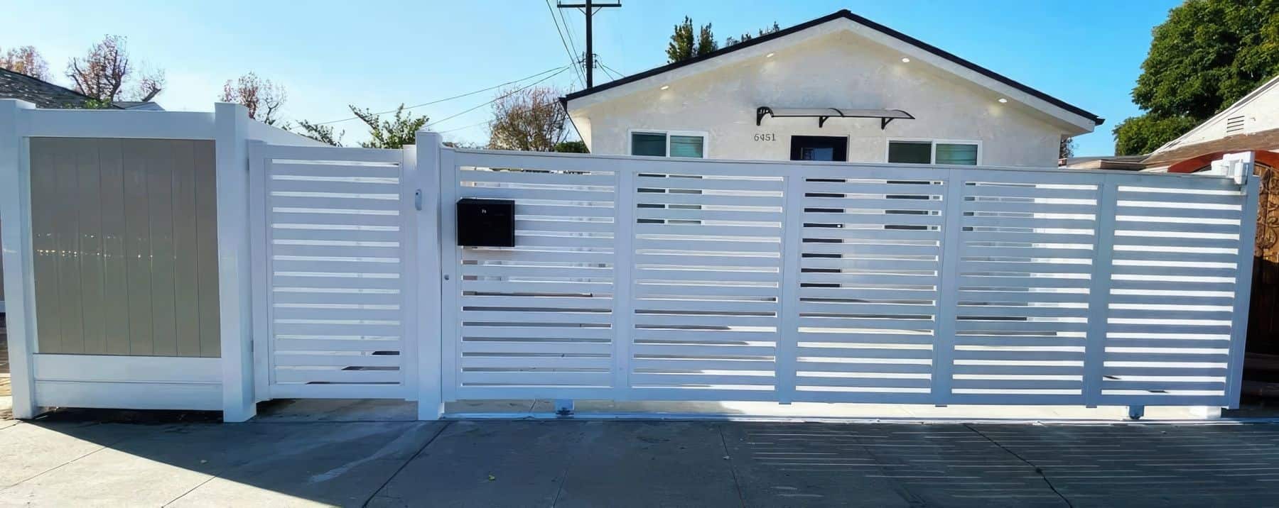 A semi-privacy vinyl rolling gate that separates the small suburban home from the sidewalk and surrounded by fences.