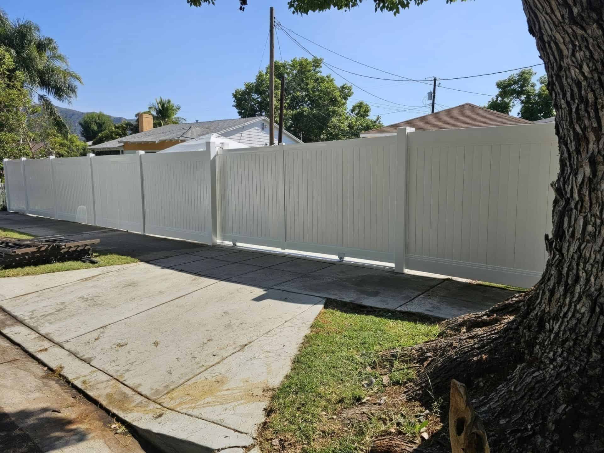 Vinyl rolling gate and fence surrounding townhouse with trees and patches of grass on each side of the entry way.