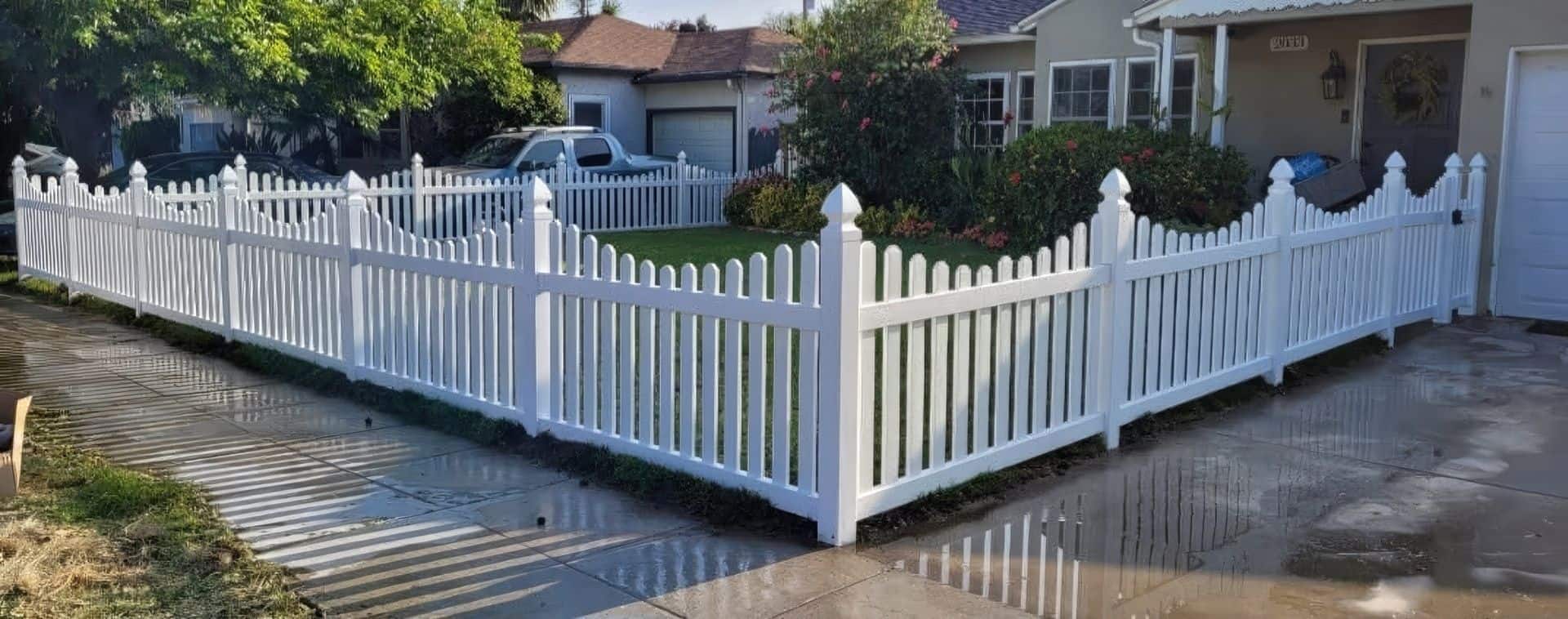 Vinyl scalloped picket fence surrounding the front lawn and entrance of cozy suburban home with a small garden