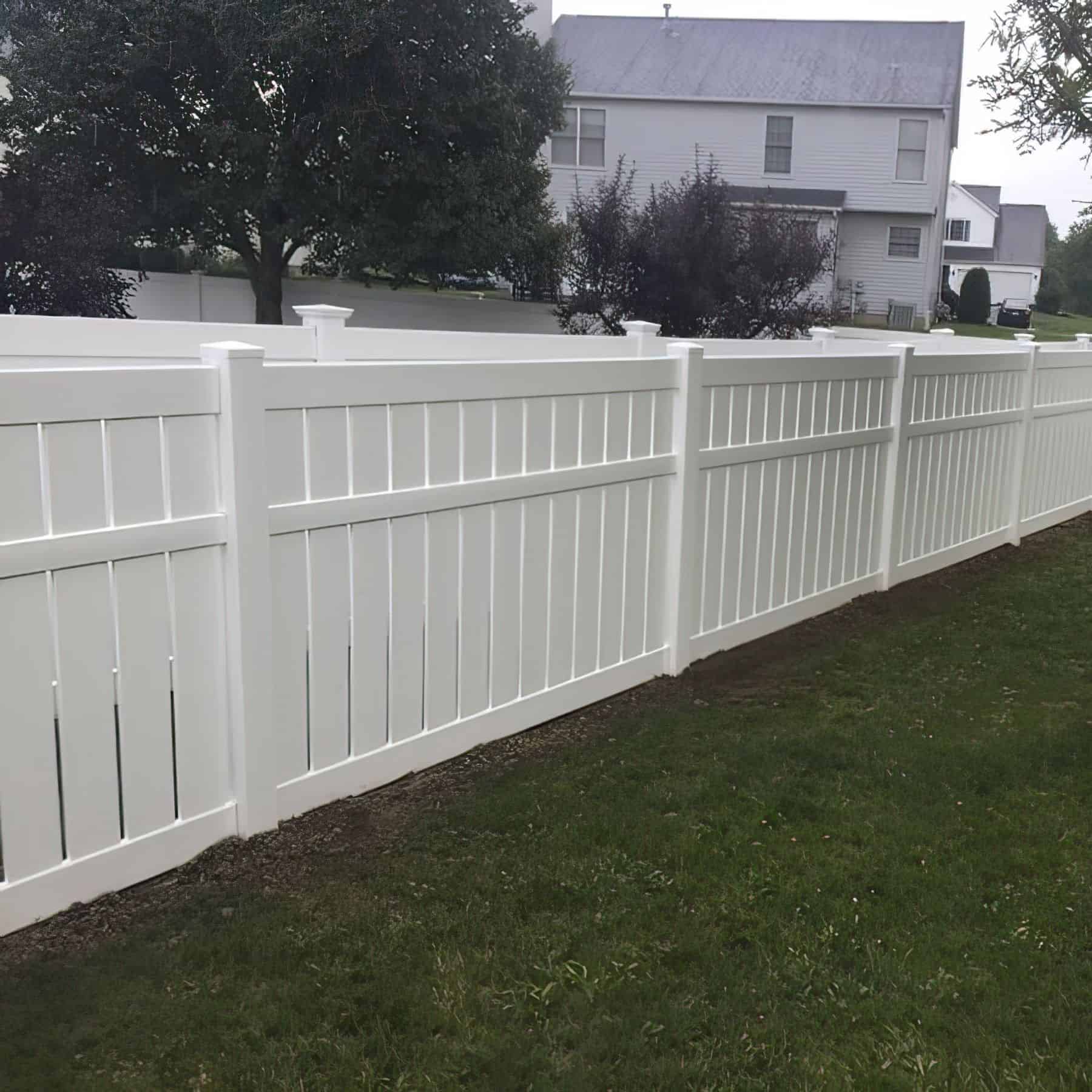 A minimalistic vinyl semi-privacy fence with stylized gaps separating two different backyards while surrounded by trees.