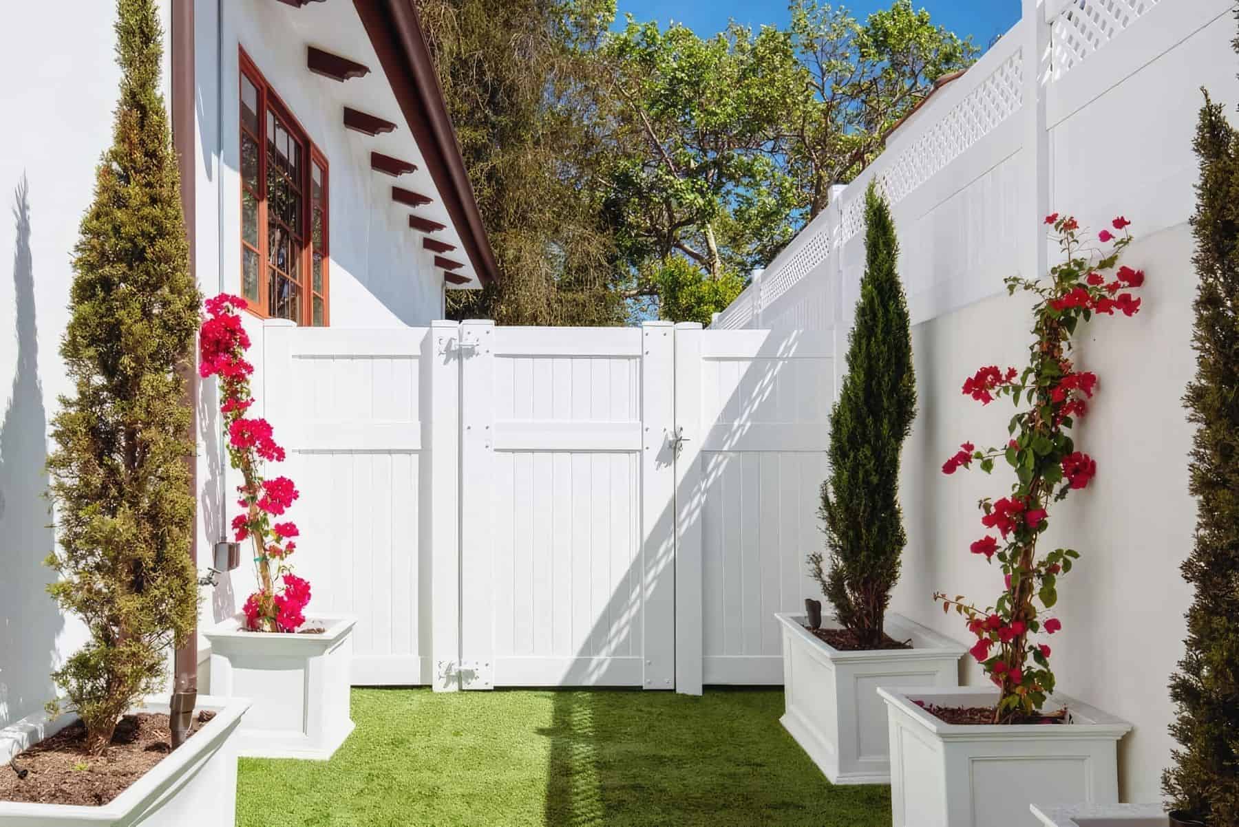 Flowers and shrubs leading up to plain white vinyl single side gate entrance leading from the front lawn to the backyard