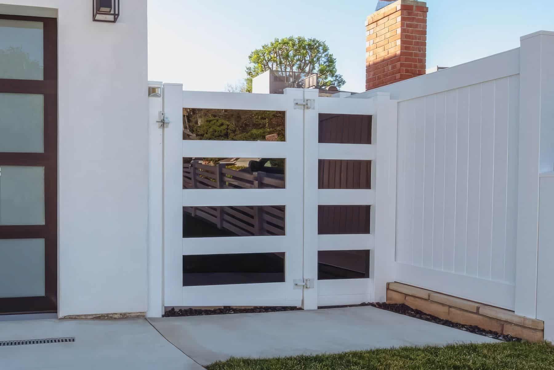 A minimalist, pure white vinyl side gate connecting the front lawn to the backyard featuring tinted reflective glass.