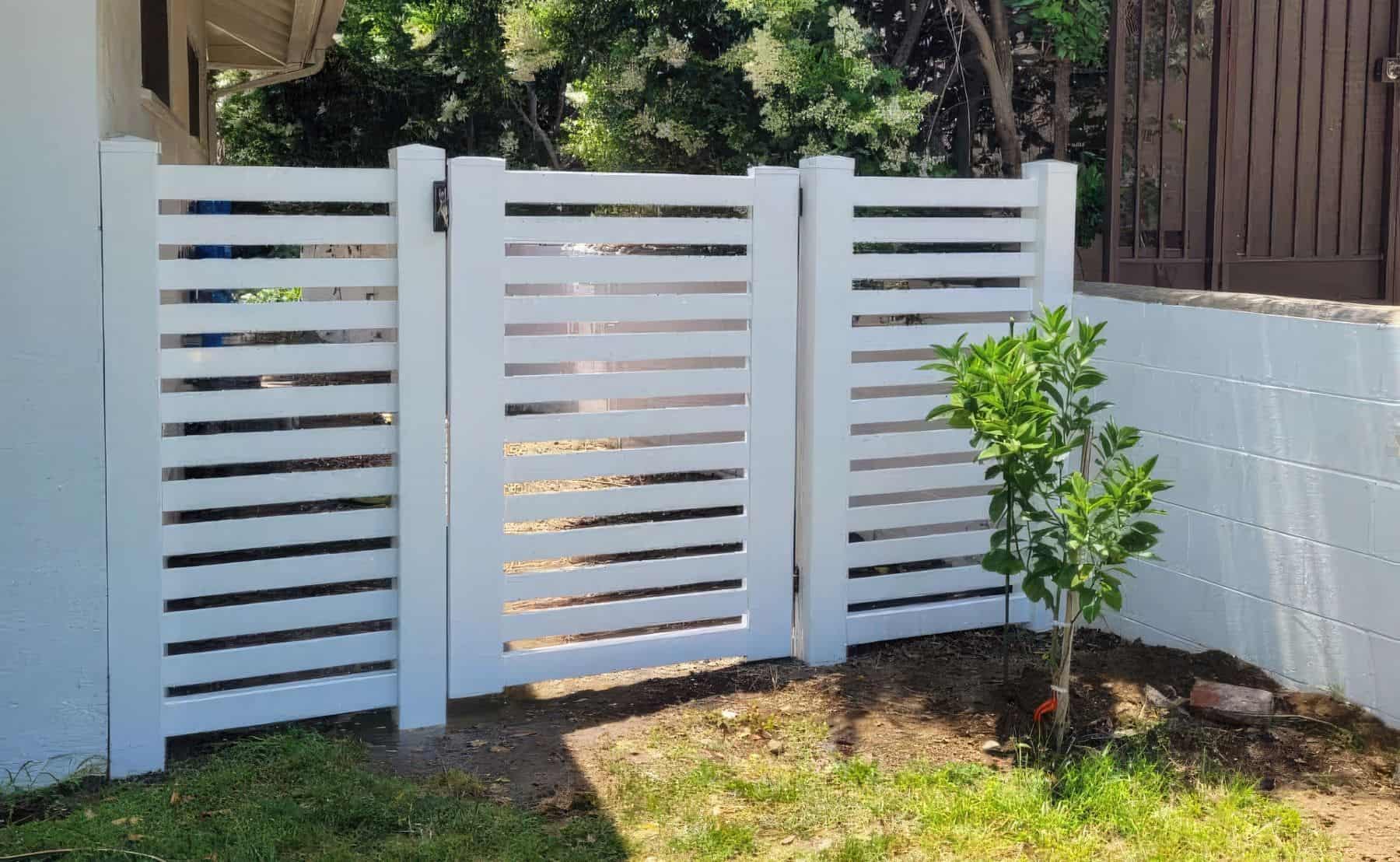 White slatted, vinyl single side gate leading into grassy backyard garden from the side passage, surrounded by trees.