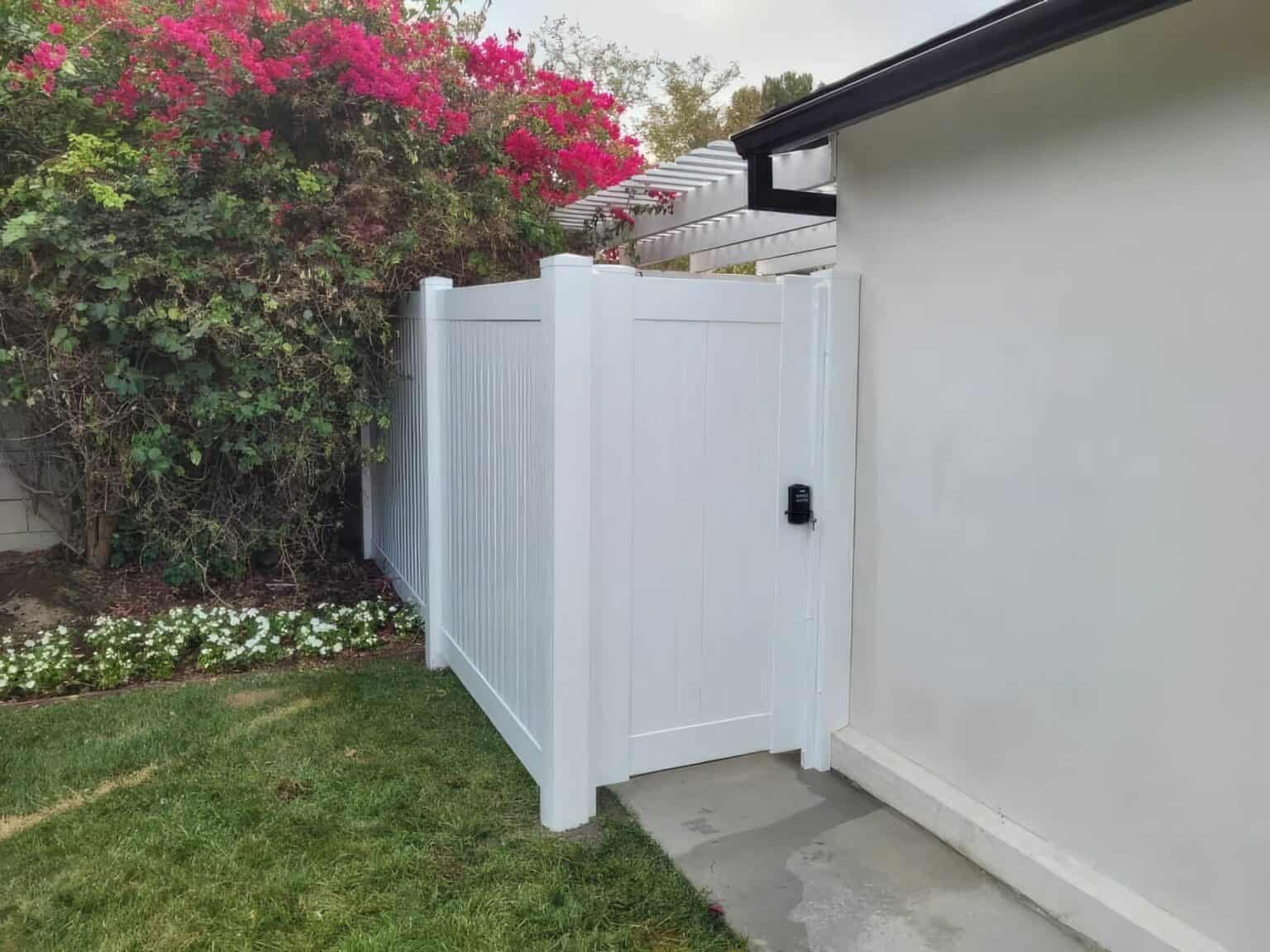 Cute white vinyl single side gate separating the grassy backyard garden from the post modern patio with a black handle.
