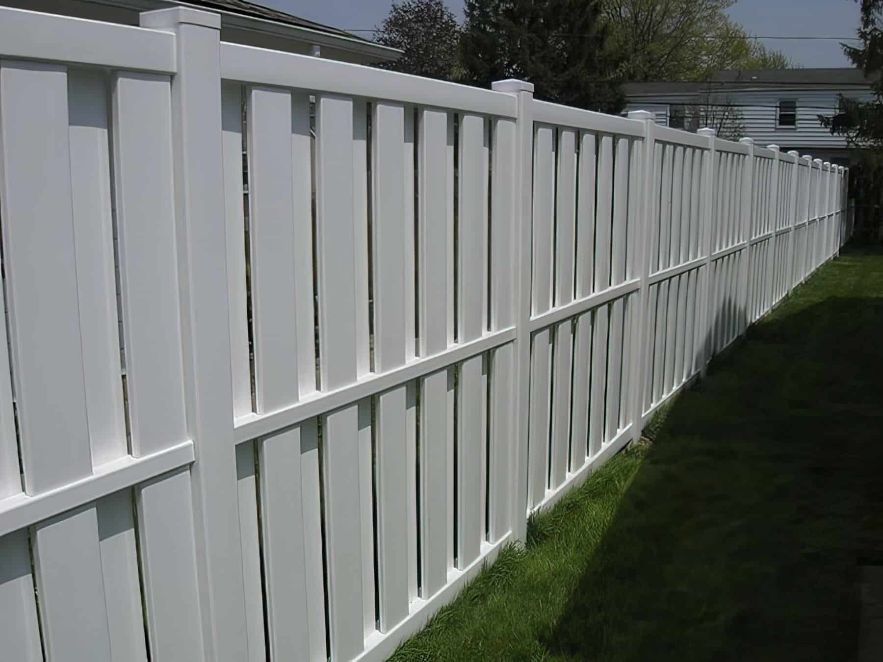 Vinyl vertical picket fence adjacent to lush green grass frames the boundary of the house.