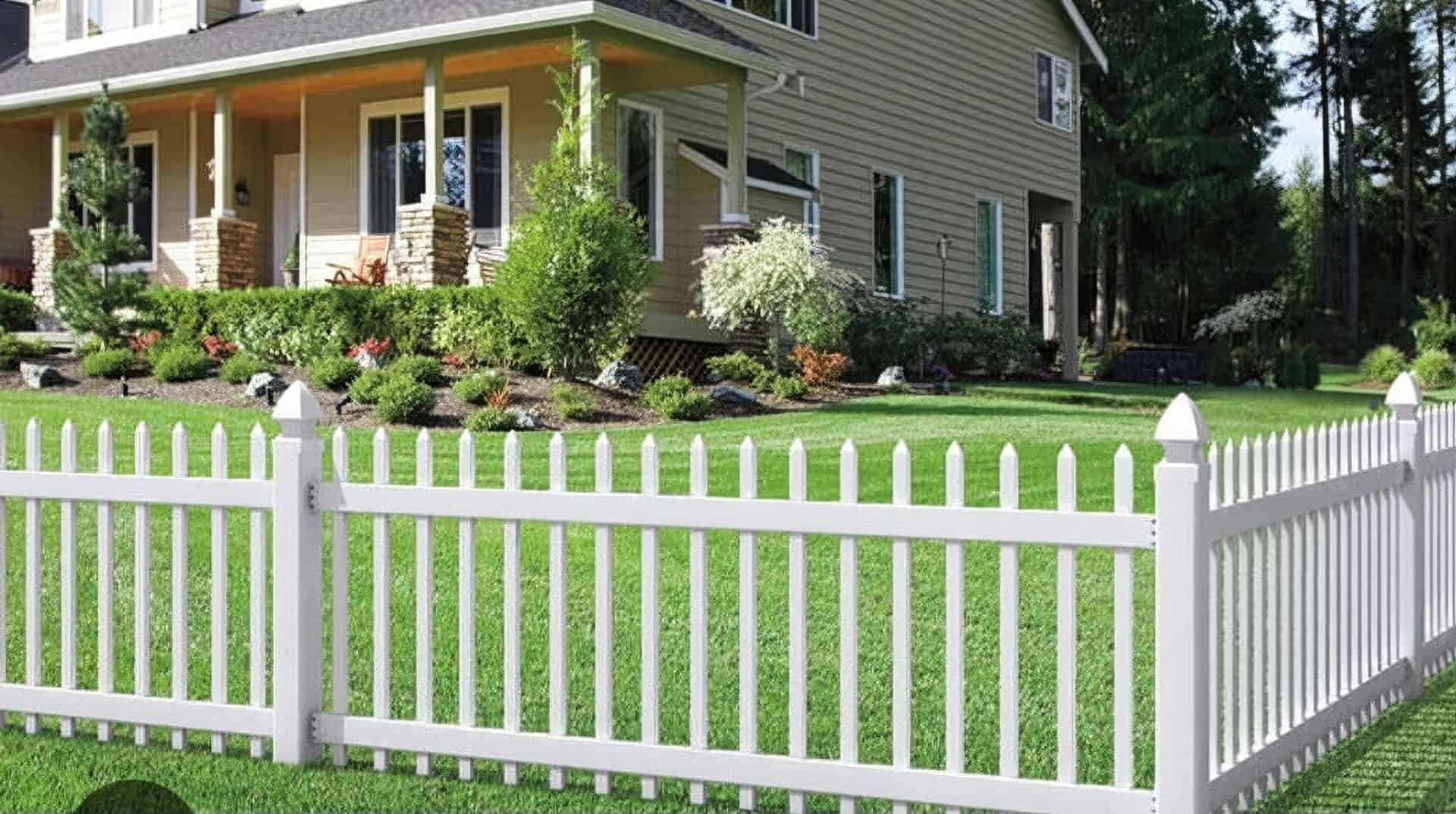 White Vinyl Vertical Picket Fence surrounding a house boundary with lush green grass and plants in the front yard.